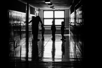 A black-and-white photograph of schoolchildren waiting in a hallway line to enter a classroom