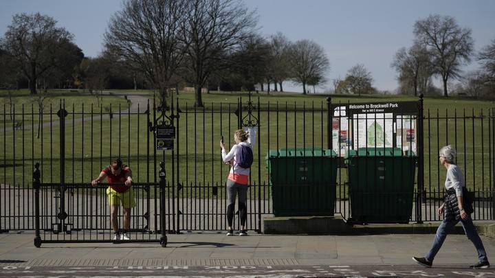 A woman removes her phone and stares through the closed gates of Brockwell Park.