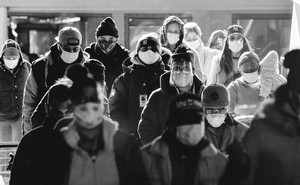 People stand together wearing masks and bundled in warm clothing.