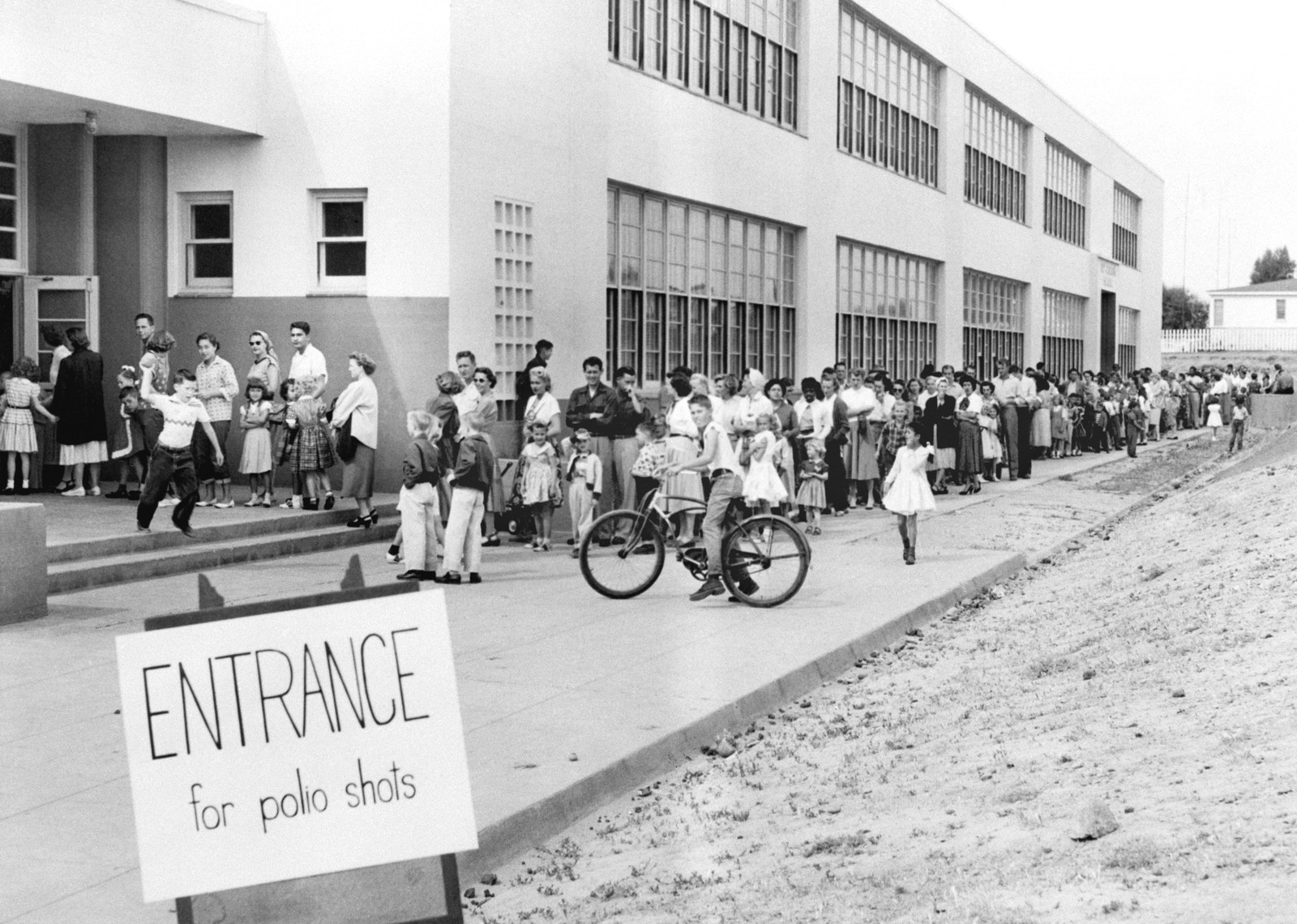 A long line of people stand outside a building, waiting for polio shots.