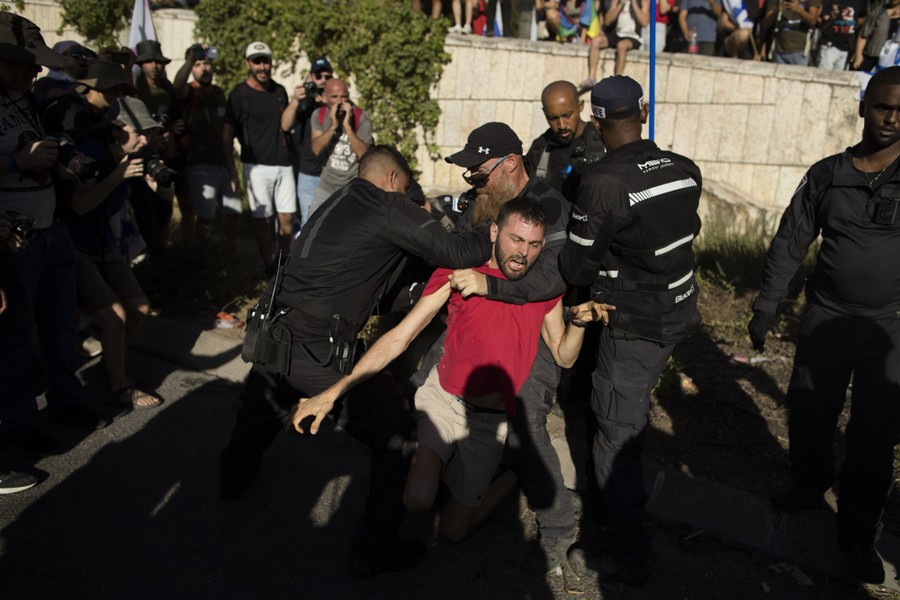 Onlookers watch as several security officers pull protesters away from a road.