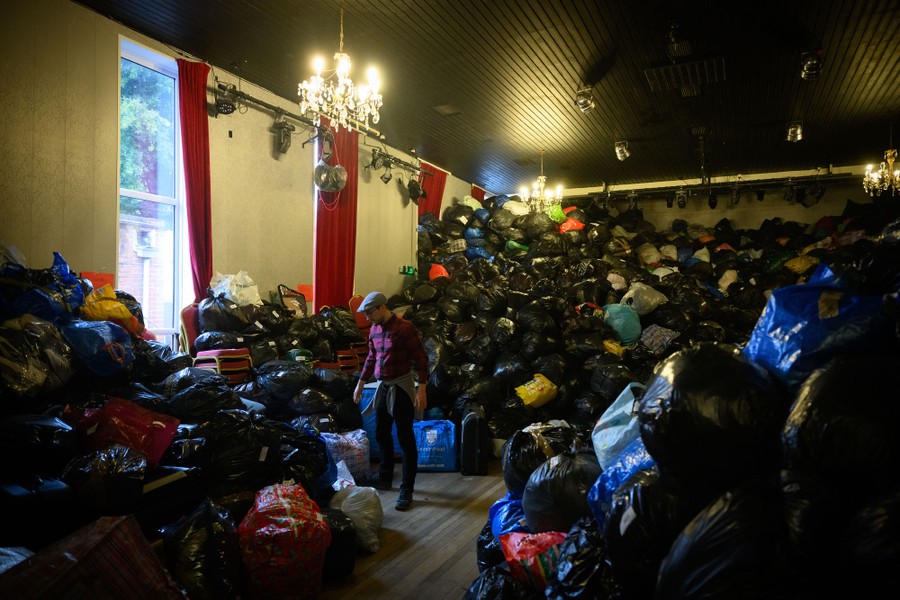 A person stands in a room surrounded by huge piles of plastic bags filled with donations meant for refugees.