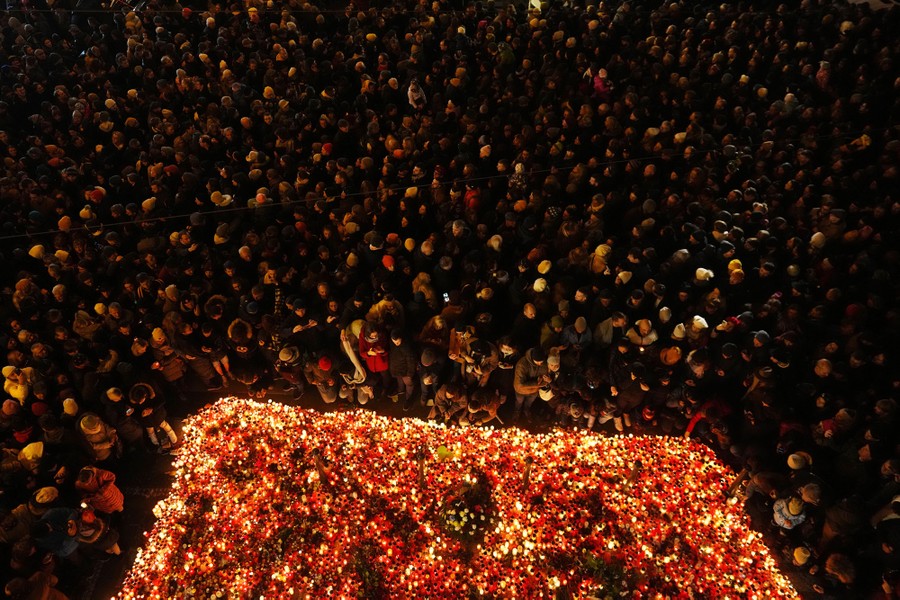 People gather around lit candles in a city square.