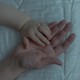 An image of an infant's hand on top of an adult's hand, both resting on a white comforter