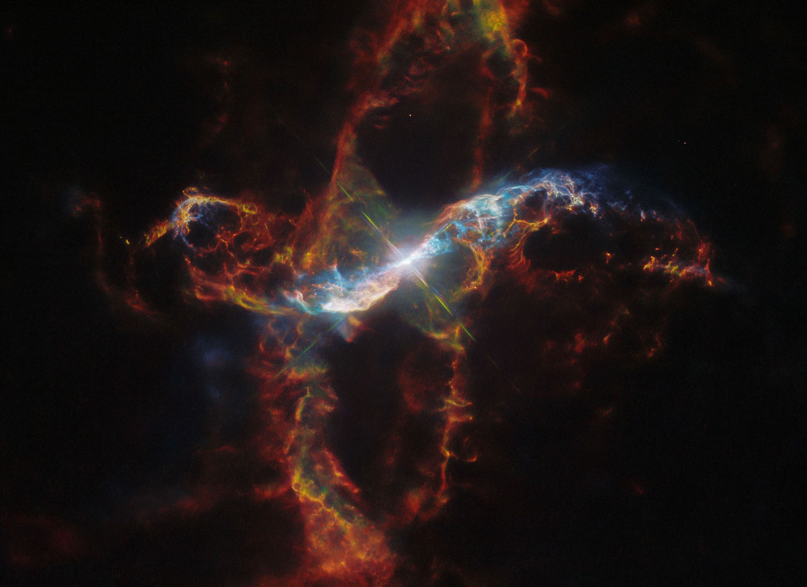 A bright binary star surrounded by a nebula. The star in the center is a large white spot surrounded by a sphere of light. The nebula extends above, below, left, and right of the star in a long arc composed of thin, multicolored filaments.