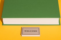 A smaller book that says "WELCOME" spread out in front of a larger book like a welcome mat