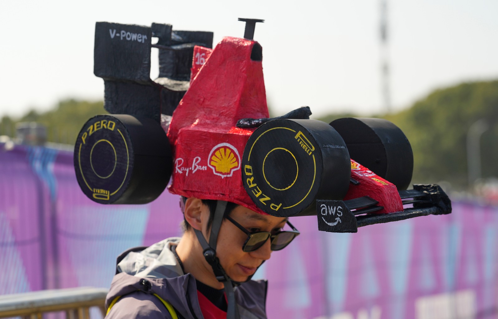 A racing fan wears a large hat shaped like an F1 race car.