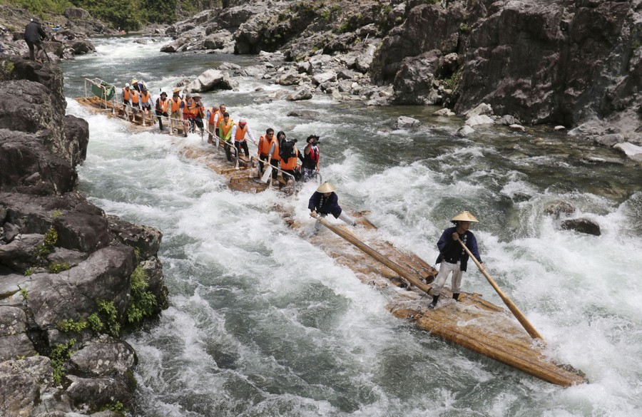 Passengers stand on long wooden rafts linked together as they float down rapids.