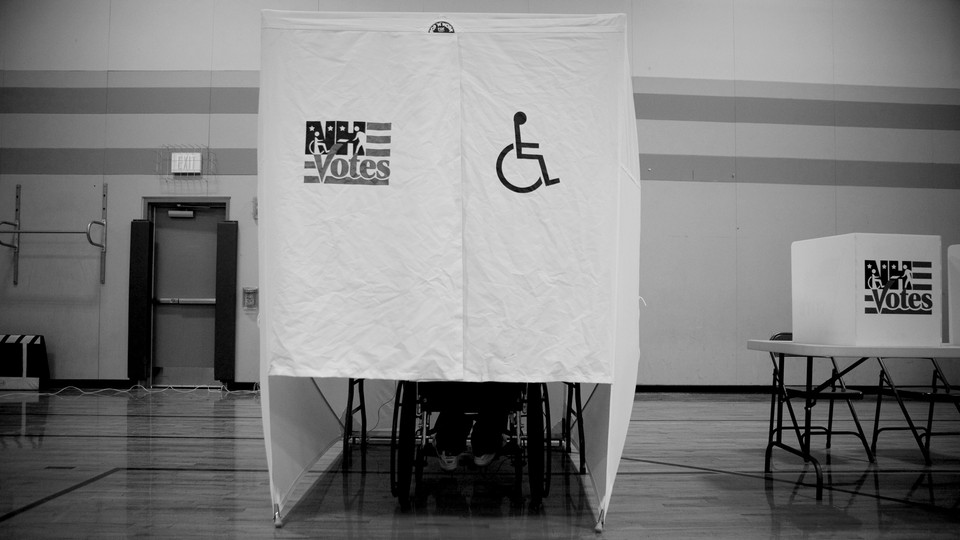 A person using a wheelchair votes at a wheelchair-accessible voting booth.