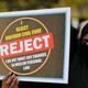 A woman in a niqab holds a placard reading "I reject uniform civil code. I do not want any changes in Muslim personal law."