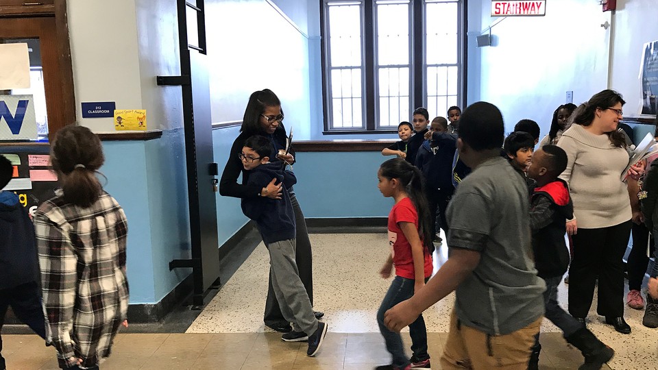 A child in a crowded hallway hugs the principal. 
