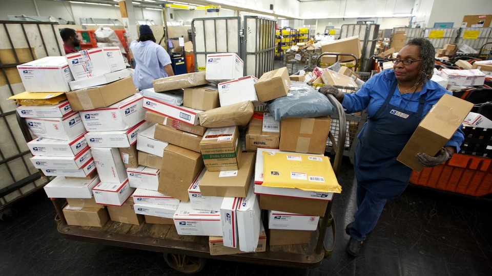 A U.S. Postal Service employee stands next to a cart full of packages.