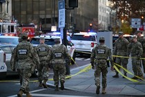 National Guardsmen in camouflage uniforms walk down a street in Washington, D.C., with yellow tape.