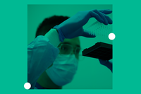 A man wearing glasses, a surgical mask, and rubber gloves examines laboratory samples in small vials.