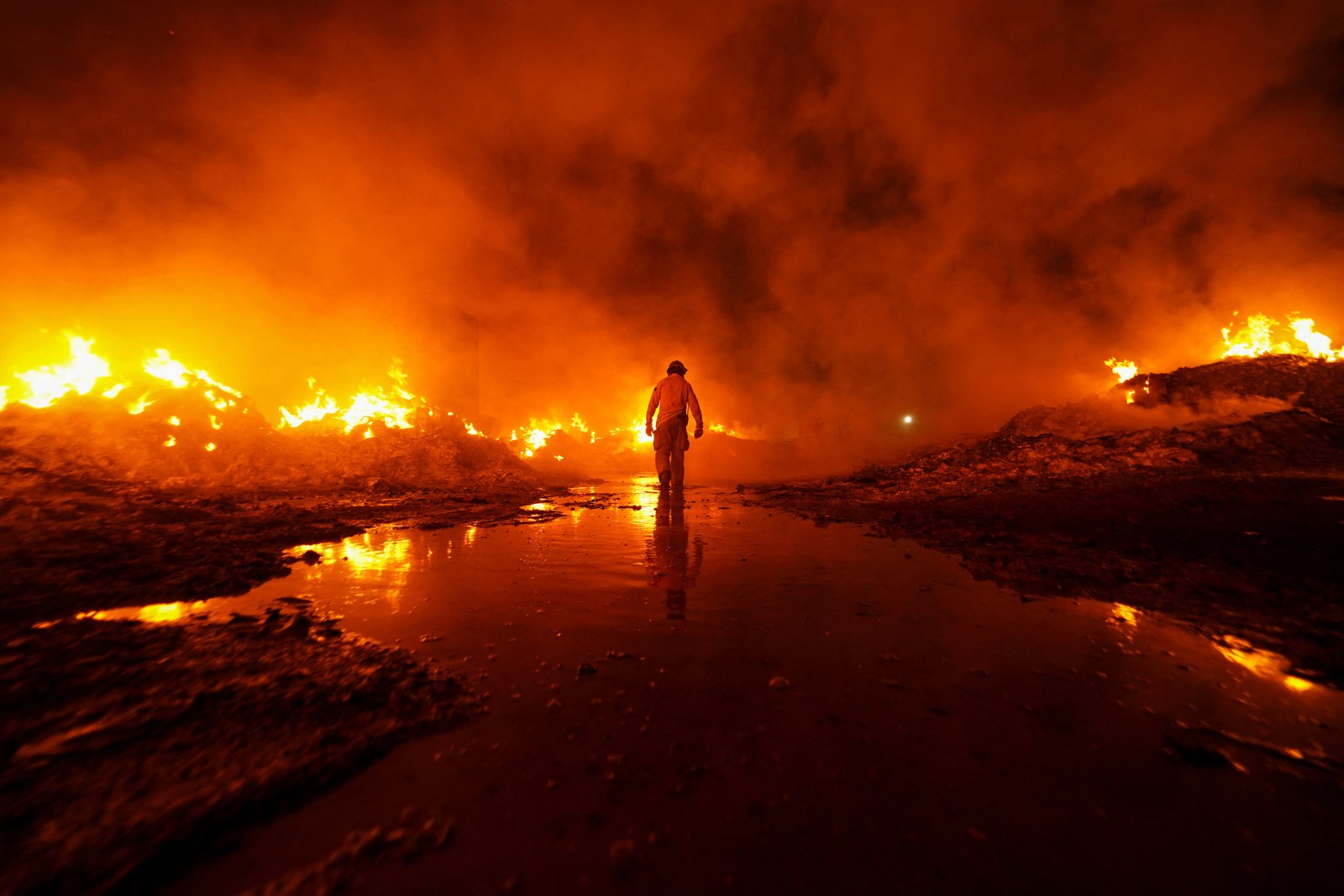 A firefighter walks amid flames in a large industrial site.