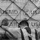 Black-and-white photograph of a person leaning against a stack of boxes labeled "USAID"