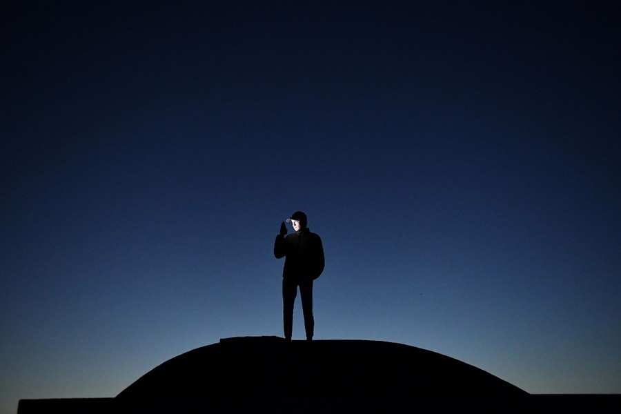 A man stands on the roof of a house at night with his phone.