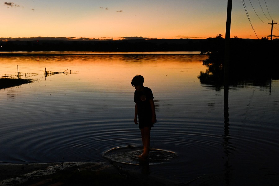 A boy wades at the edge of a broad floodplain.