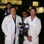 Two doctors in white coats stand in front of microphones