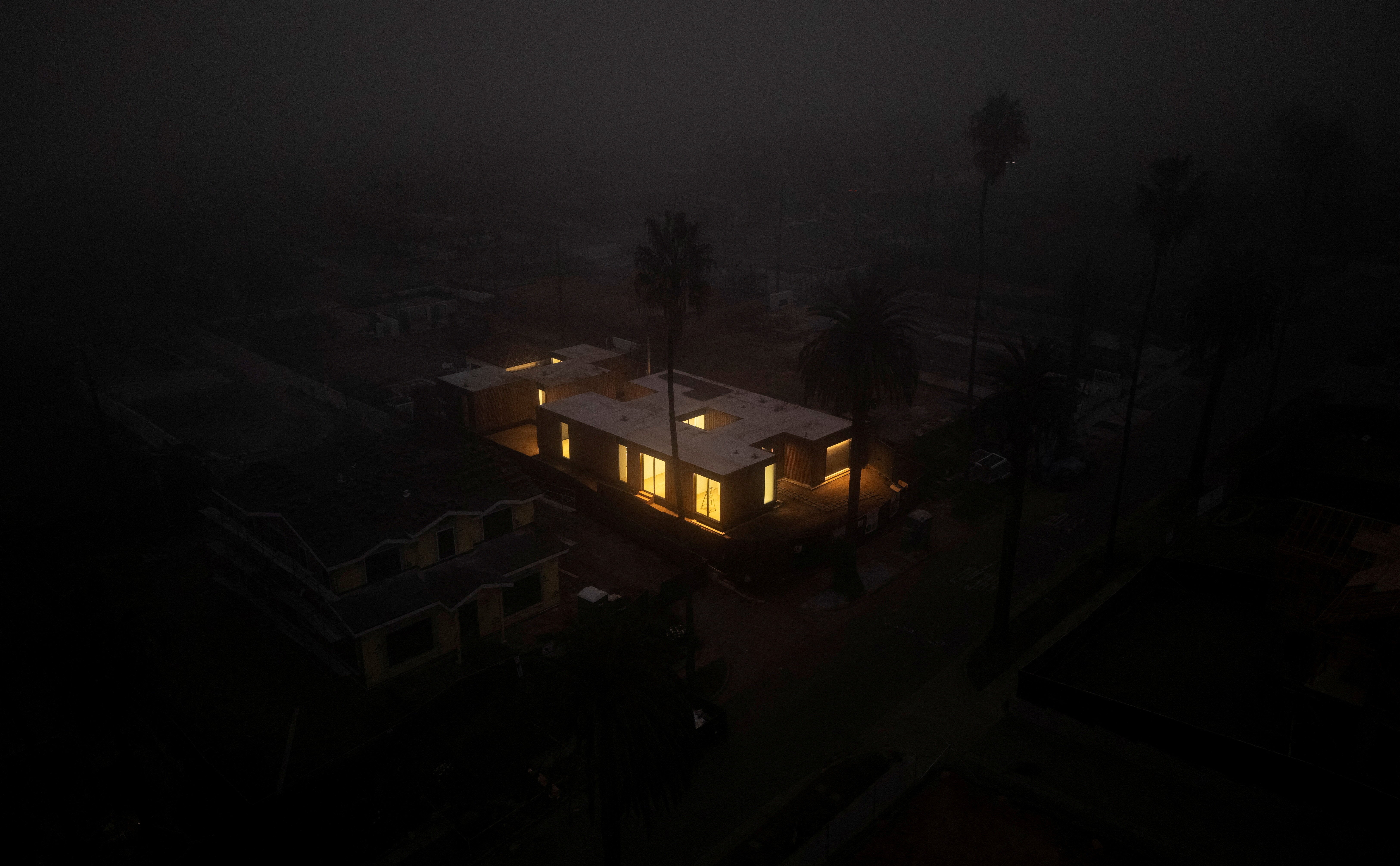 An aerial view, on a dark foggy night, of a house under construction, lit from within