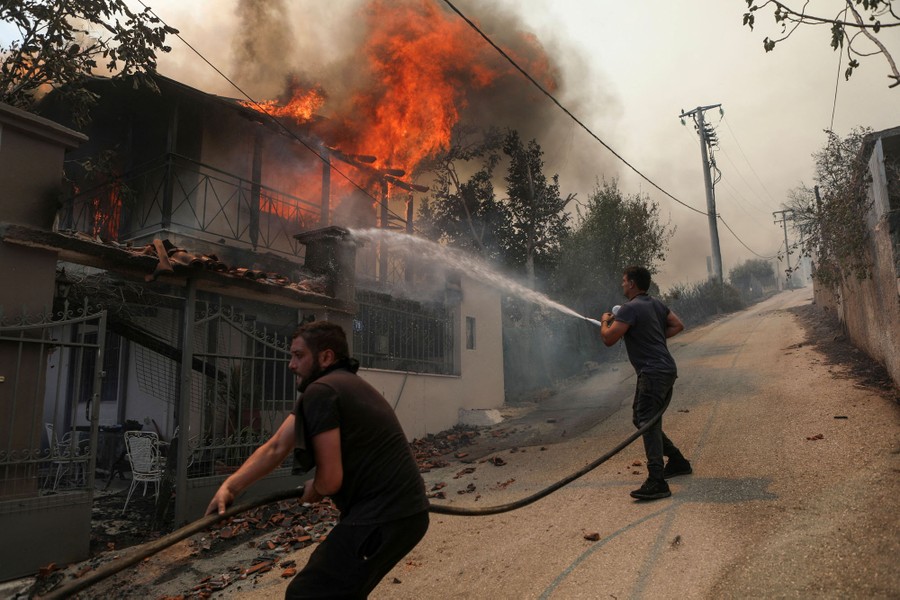 Two people use a hose to spray water on a burning house.