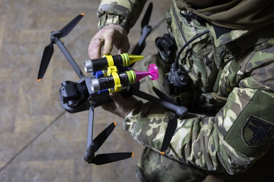 A soldier secures two grenades to a small drone.