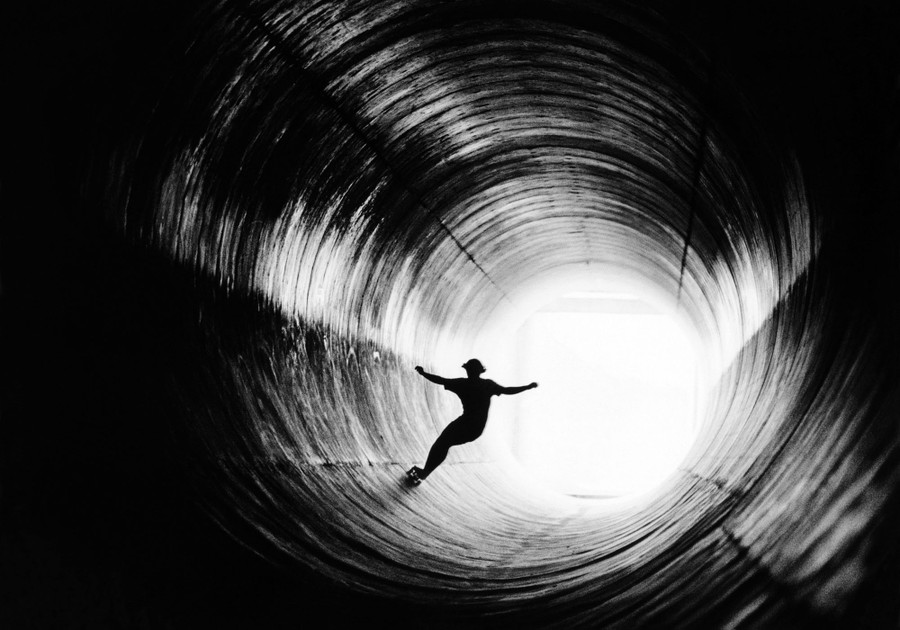 A skateboarder rides through a large concrete storm drain.