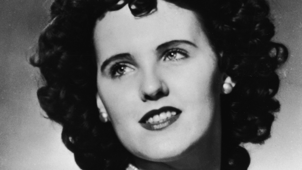 A close-up black and white photo of a smiling woman with light eyes and dark hair.