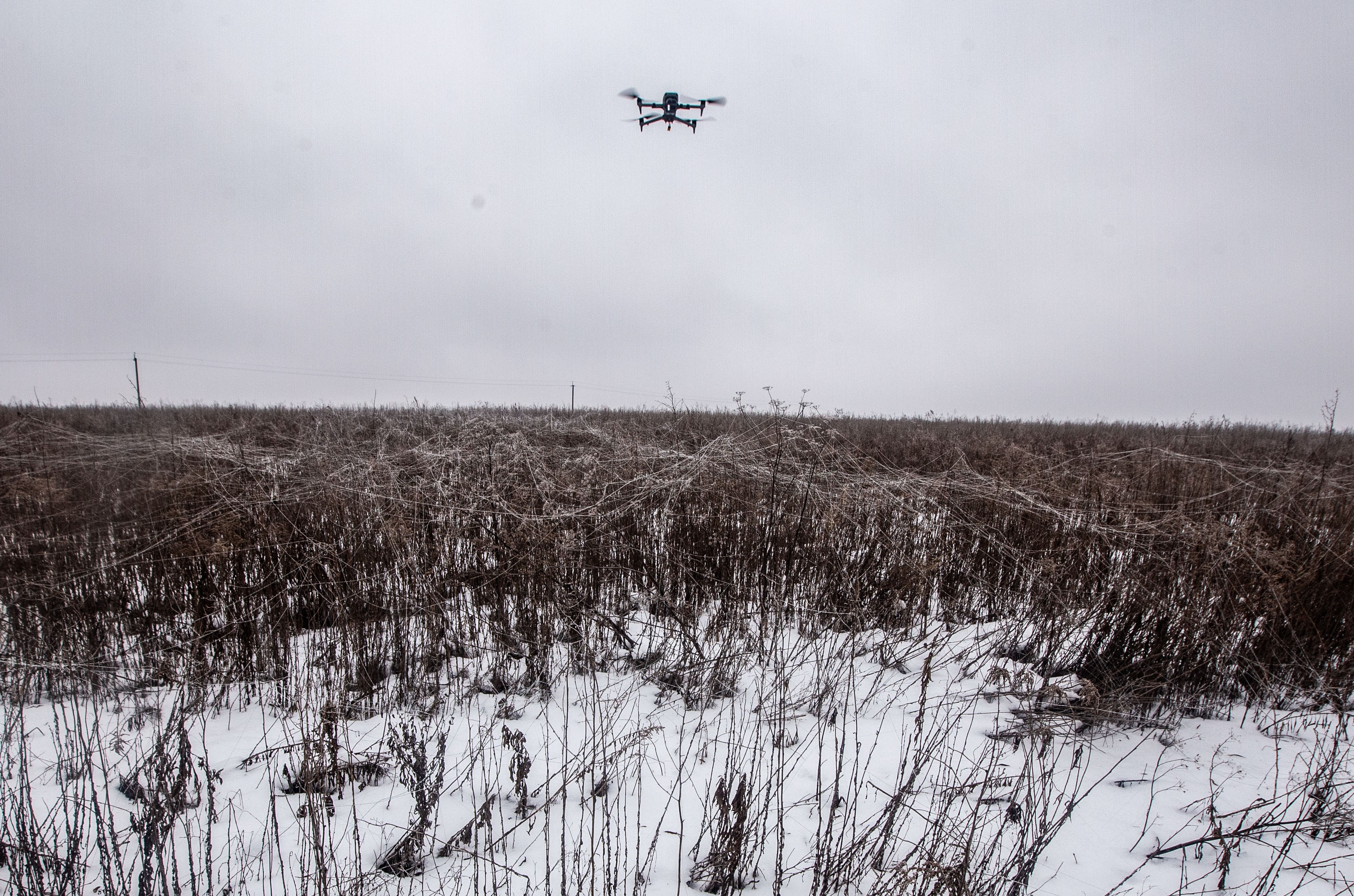 A small reconnaissance drone flies above a field covered by discarded fiber-optic drone fibers.