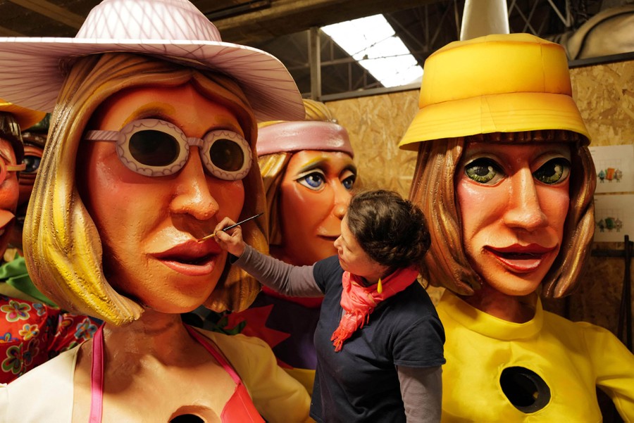 An artist uses a paintbrush to work on large figurines made for a parade.