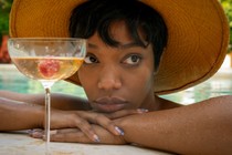 Naomi Ackie peering over the side of a pool next to a cocktail