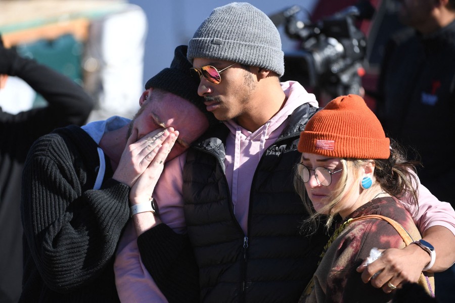 Several people embrace each other at a memorial.
