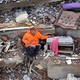 A man sits in the rubble of a collapsed building, his left arm reaching out and holding the hand of his daughter, who lies dead, trapped beneath the debris.