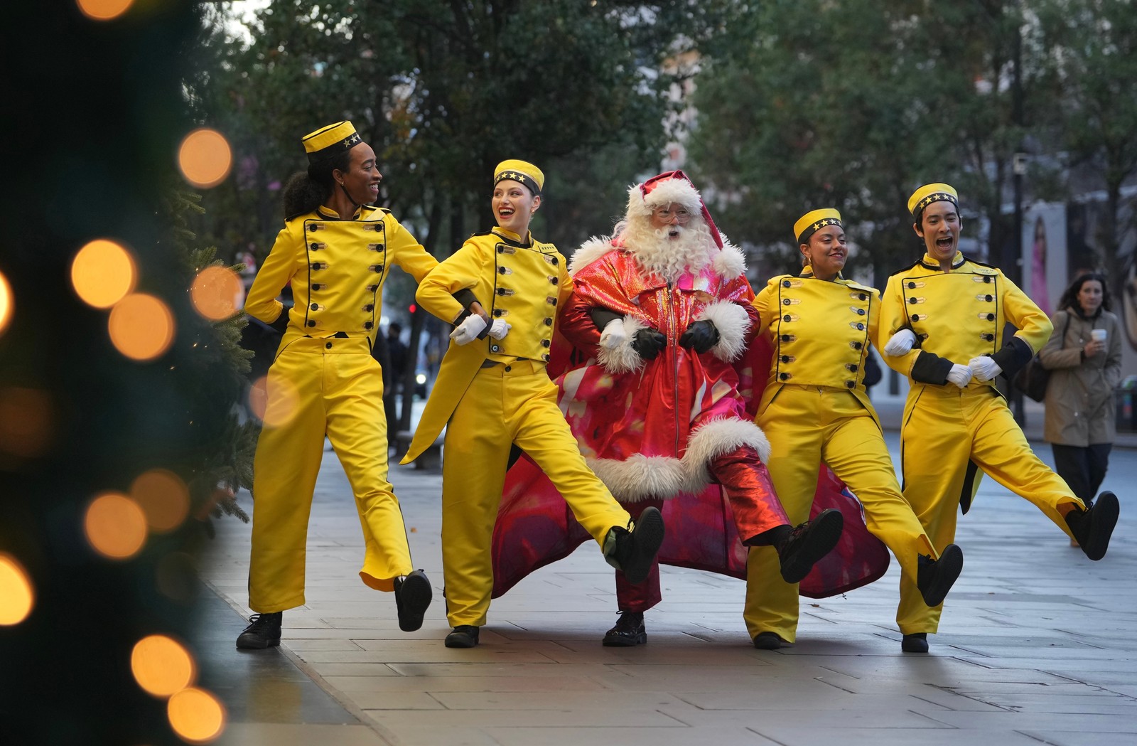 Five performers - four in bellhop costumes, one in a Santa Claus costume - kick while walking side-by-side.