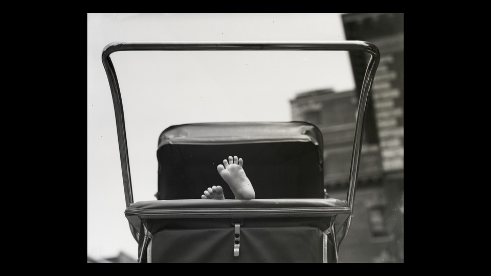 A baby's feet stick out of a stroller in a black-and-white photo.