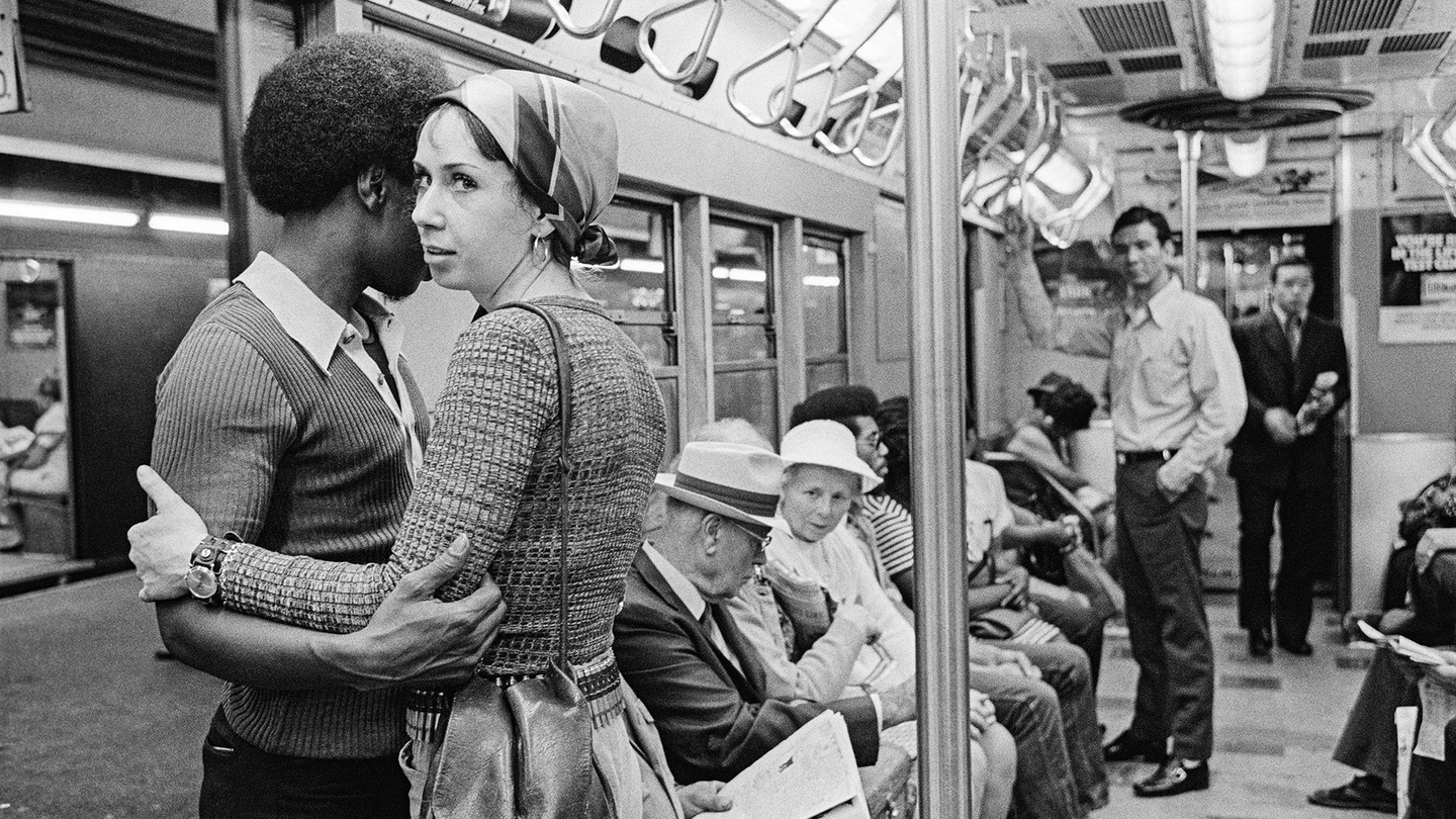 Black-and-white photograph of a couple holding each other on a crowded subway car