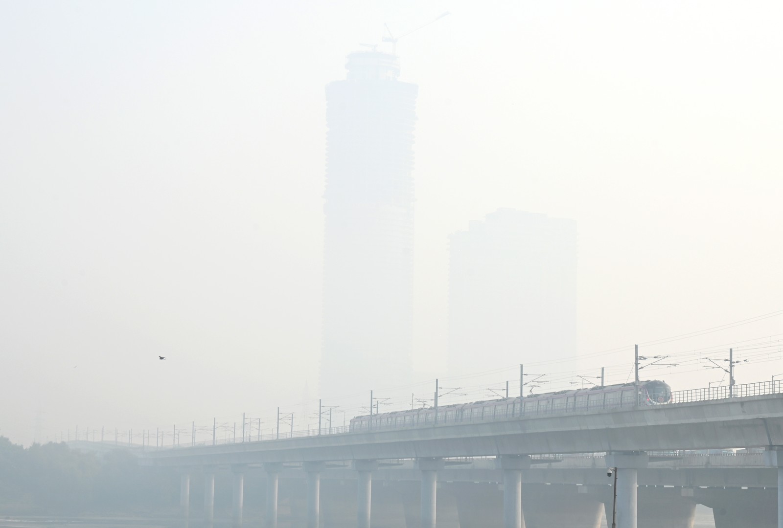A view of a train passing over a bridge and distant tall buildings on a very smoggy day