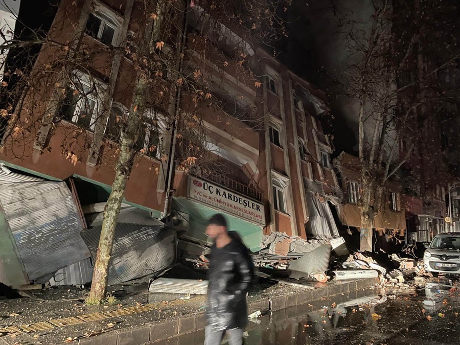 A person walks on a street past a partially collapsed three-story building.