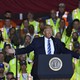 Trump gives a speech in front of workers wearing yellow vests.