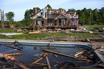 Debris floats in a pool near a severely storm-damaged house.