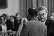 Fotografía en blanco y negro de Bill Barr y Ben Carson conversando, con la audiencia de fondo.