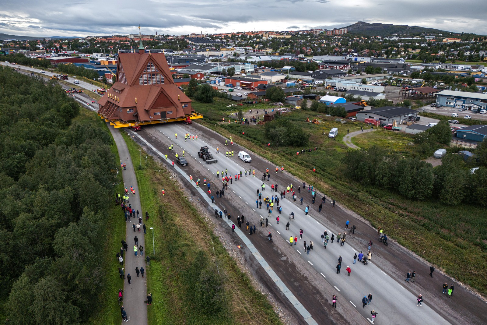 An aerial view of onlookers and workers on a road as a tall church is rolling slowly along.