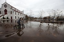A person rides a bicycle past a church on a flooded street.