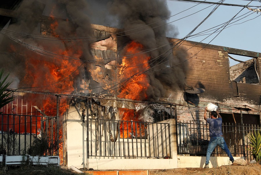 A person tosses a bucketful of water at a burning building.