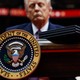 Photograph of Donald Trump behind a desk with the presidential seal and executive orders atop the desk