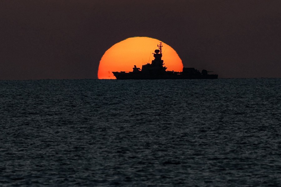A warship is silhouetted by the setting sun.