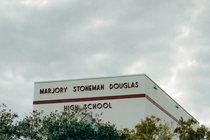 photo of building with "Marjory Stoneman Douglas High School" on it, behind trees against cloudy gray sky