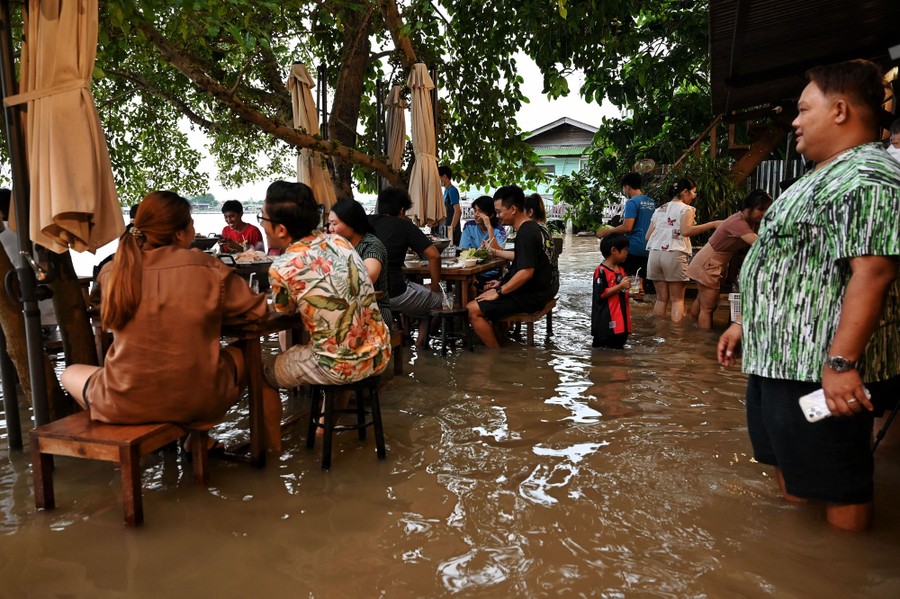 Diners eat at outdoor tables in knee-deep floodwater.