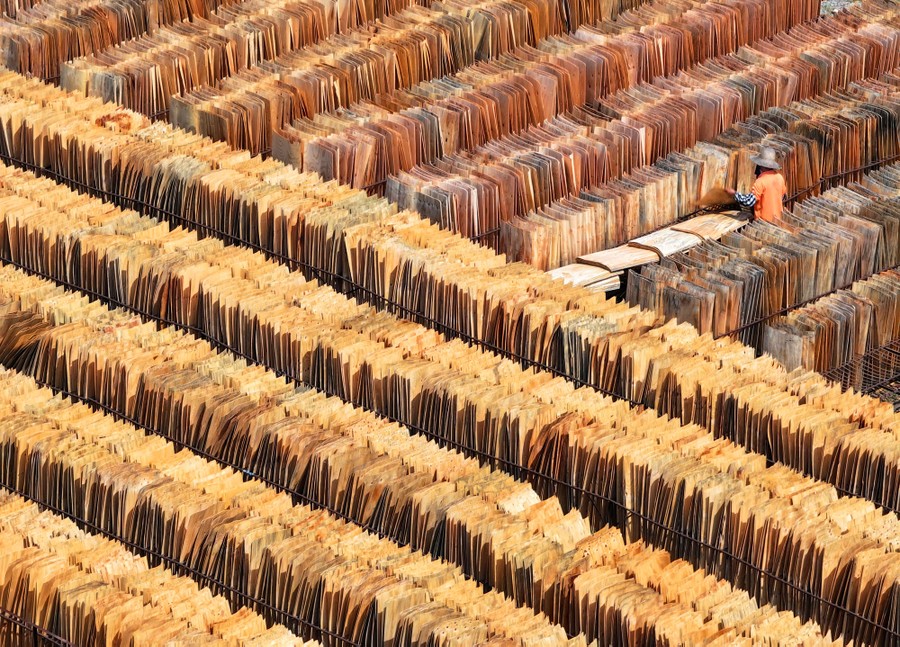 An aerial view of a person arranging slabs of wood, among many rows of stacked wood