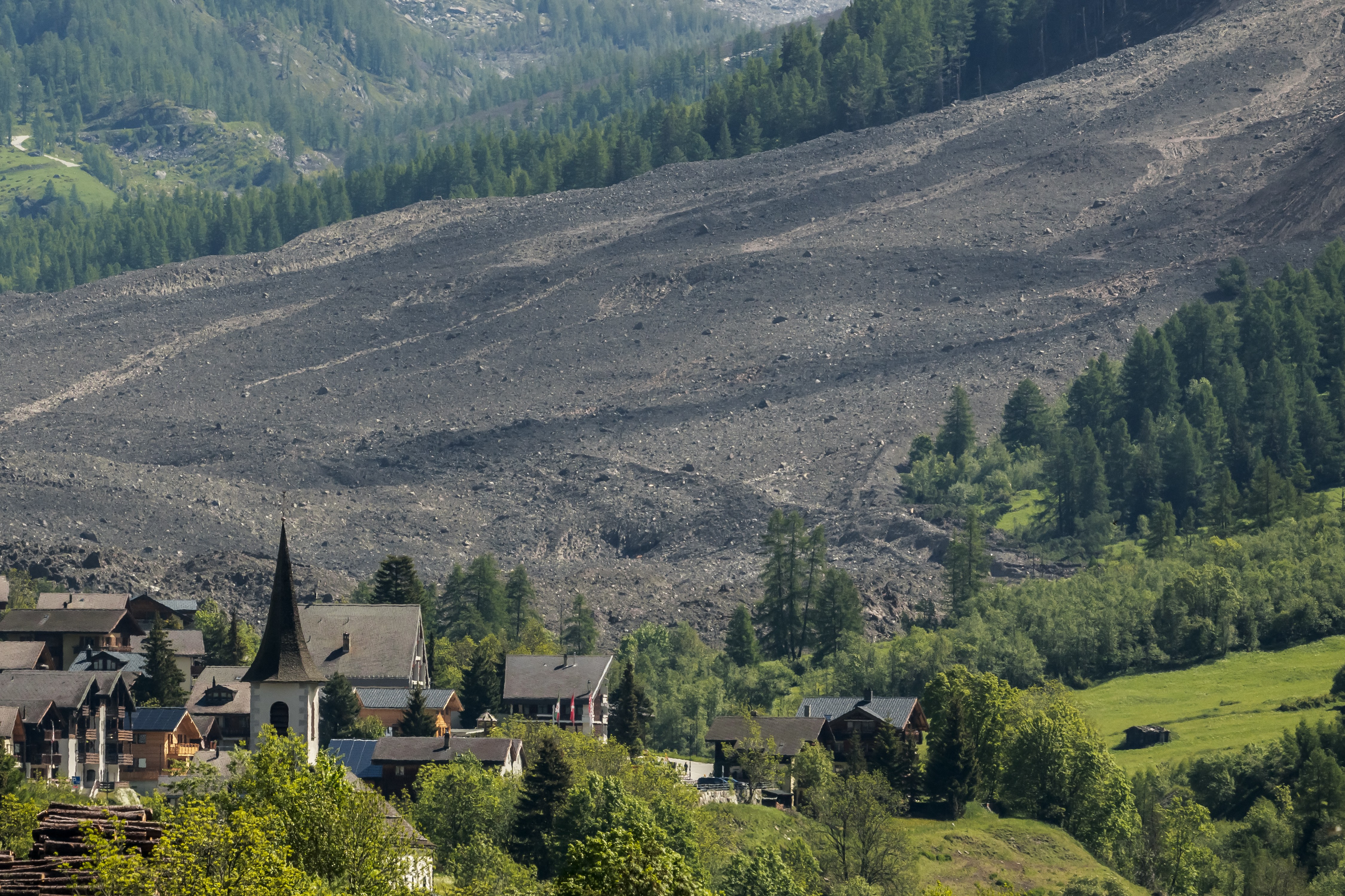 A field of landslide debris fills a valley uphill from a village.